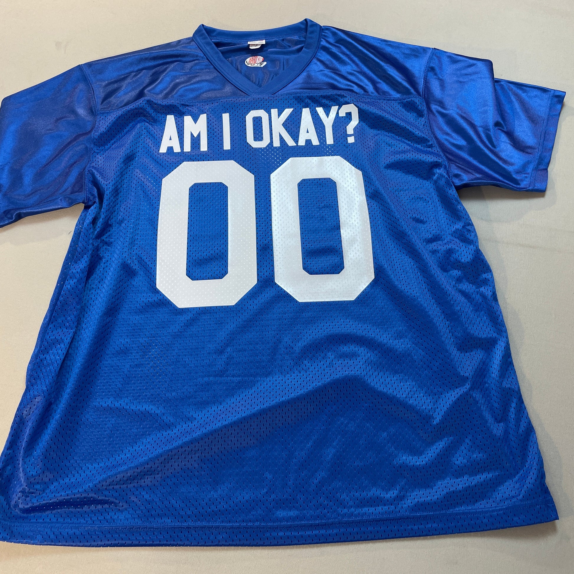 Blue sports jersey with 'AM I OKAY?' text and numbers on a beige surface